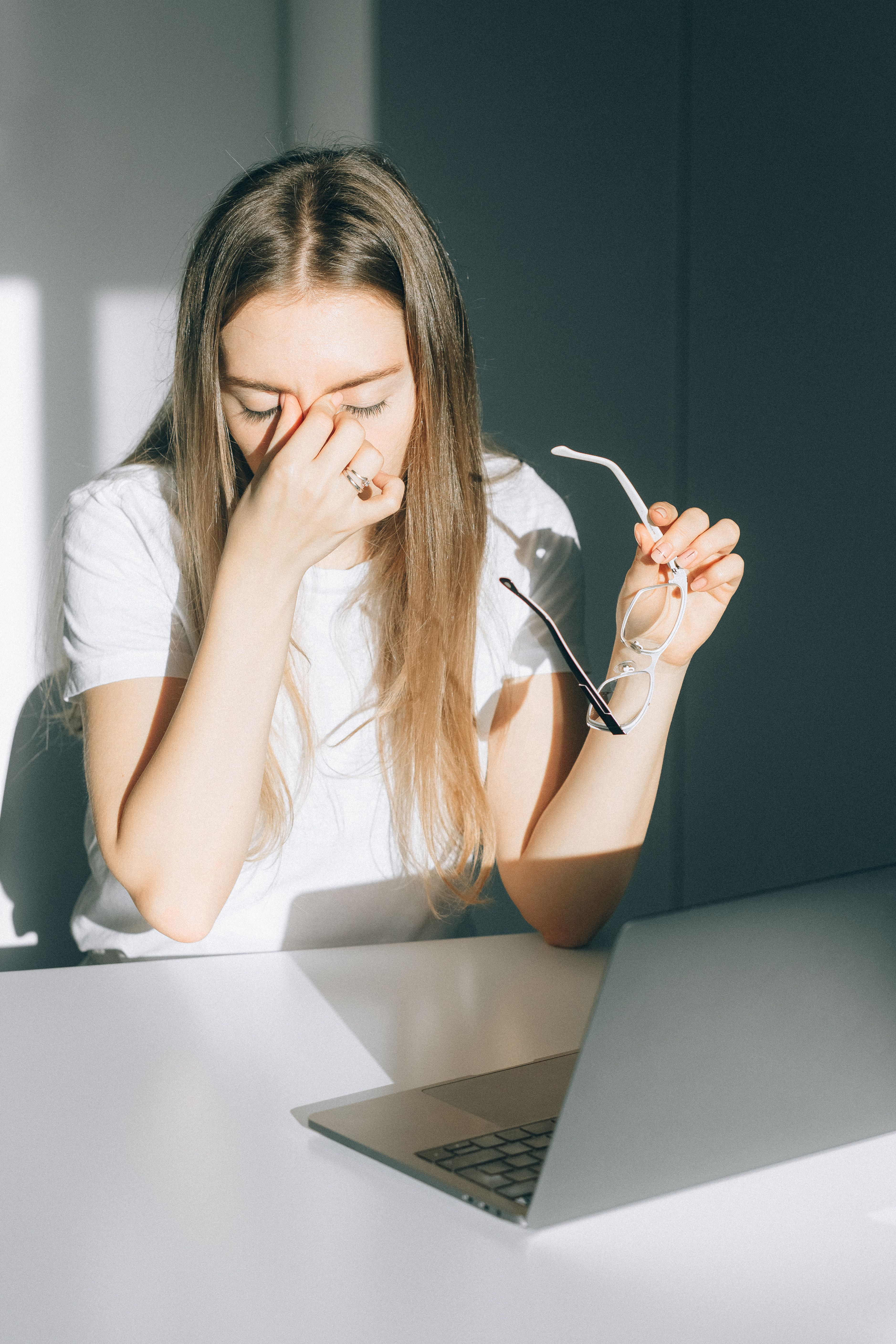 Mujer cansada frente a una computadora, sosteniendo sus anteojos y presionando el entrecejo